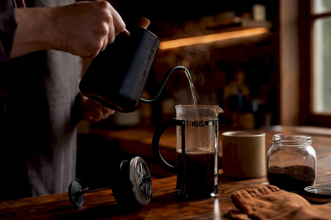 Hand pouring water over coffee grounds in French Press