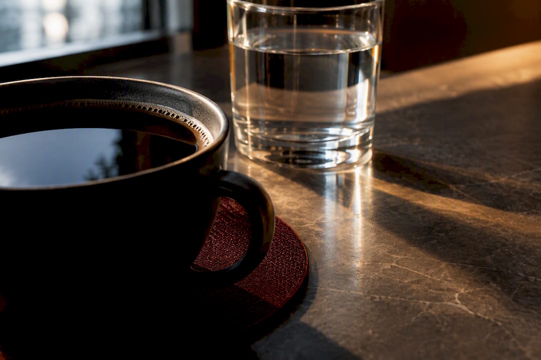 Black coffee beside water in morning light